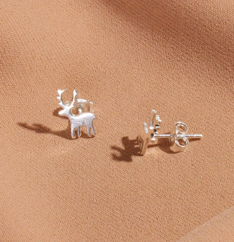 Silver deer-shaped earrings on a beige fabric background