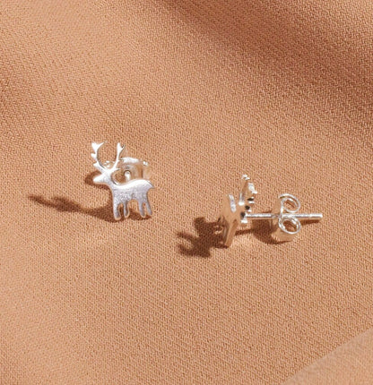 Silver deer-shaped earrings on a beige fabric background