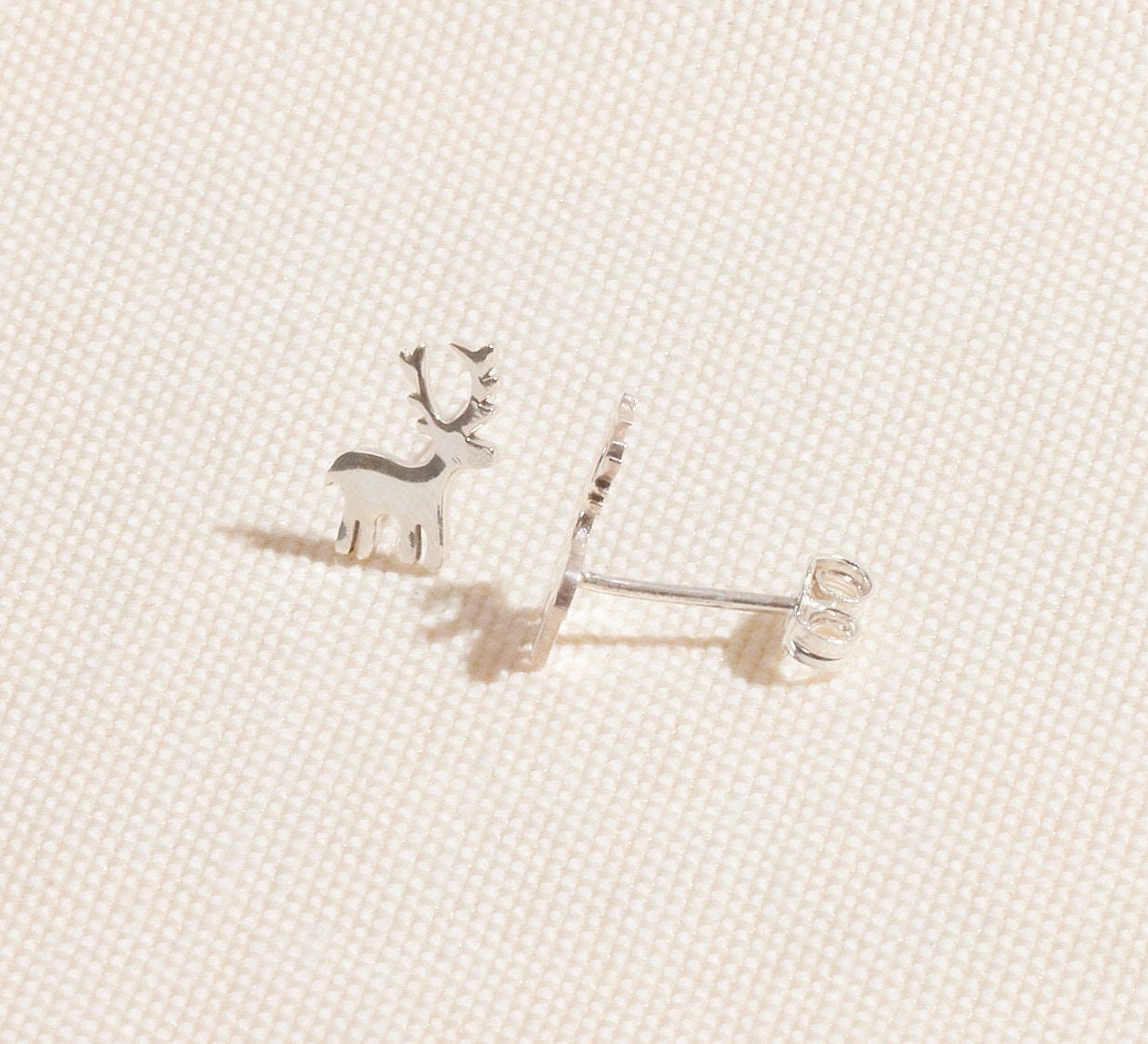 Silver reindeer-shaped earrings on a light beige fabric background