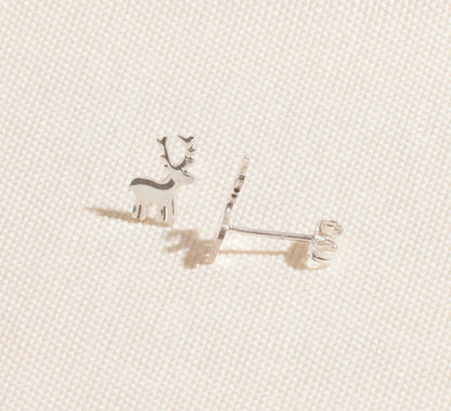 Silver reindeer-shaped earrings on a light beige fabric background