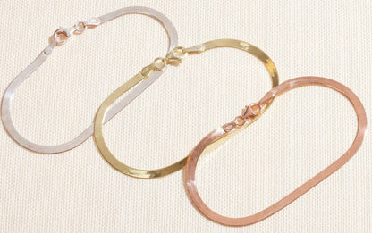 Three hoop earrings in gold, silver, and rose gold on a textured beige background
