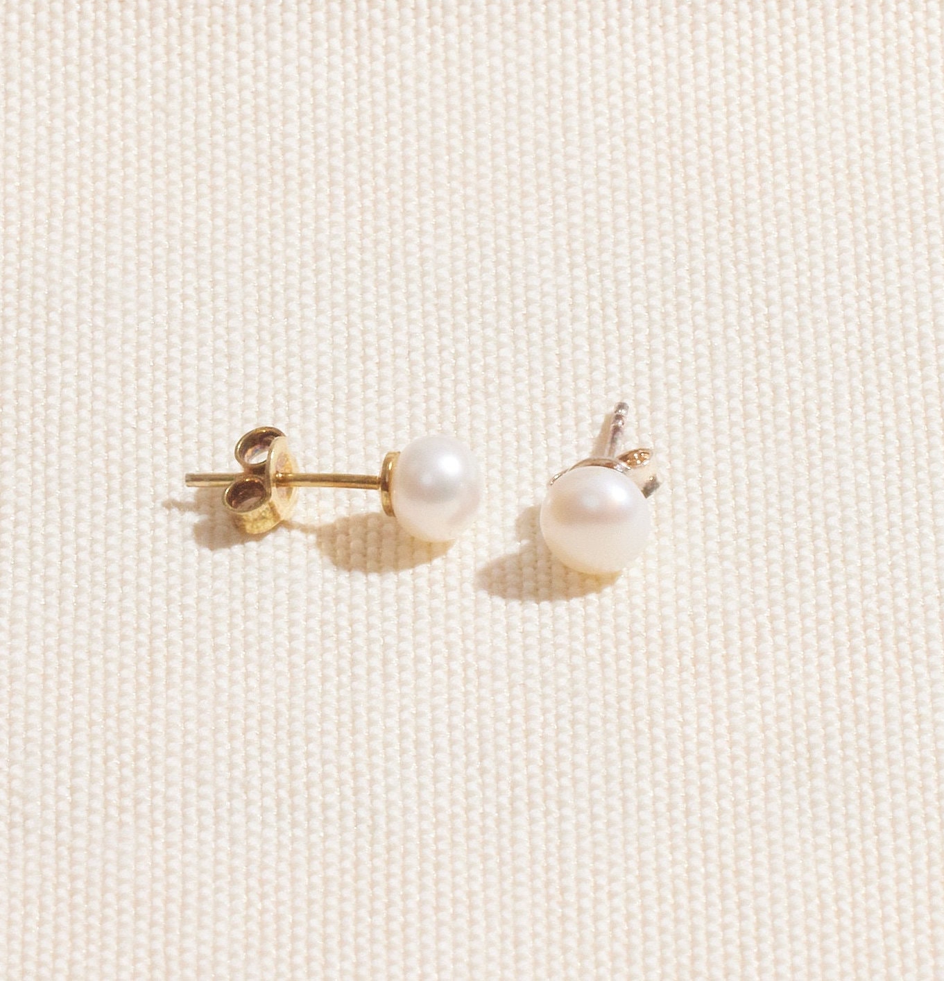 A pair of gold-colored pearl stud earrings placed on a white surface.