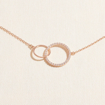Rose gold necklace with interlocking rings on a light beige background