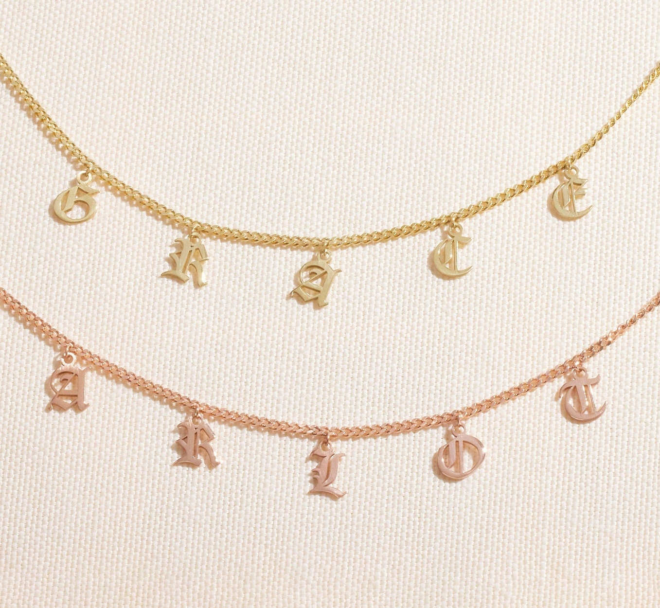 Personalized name necklace featuring Gothic dangle letters in gold and rose gold curb chain design.