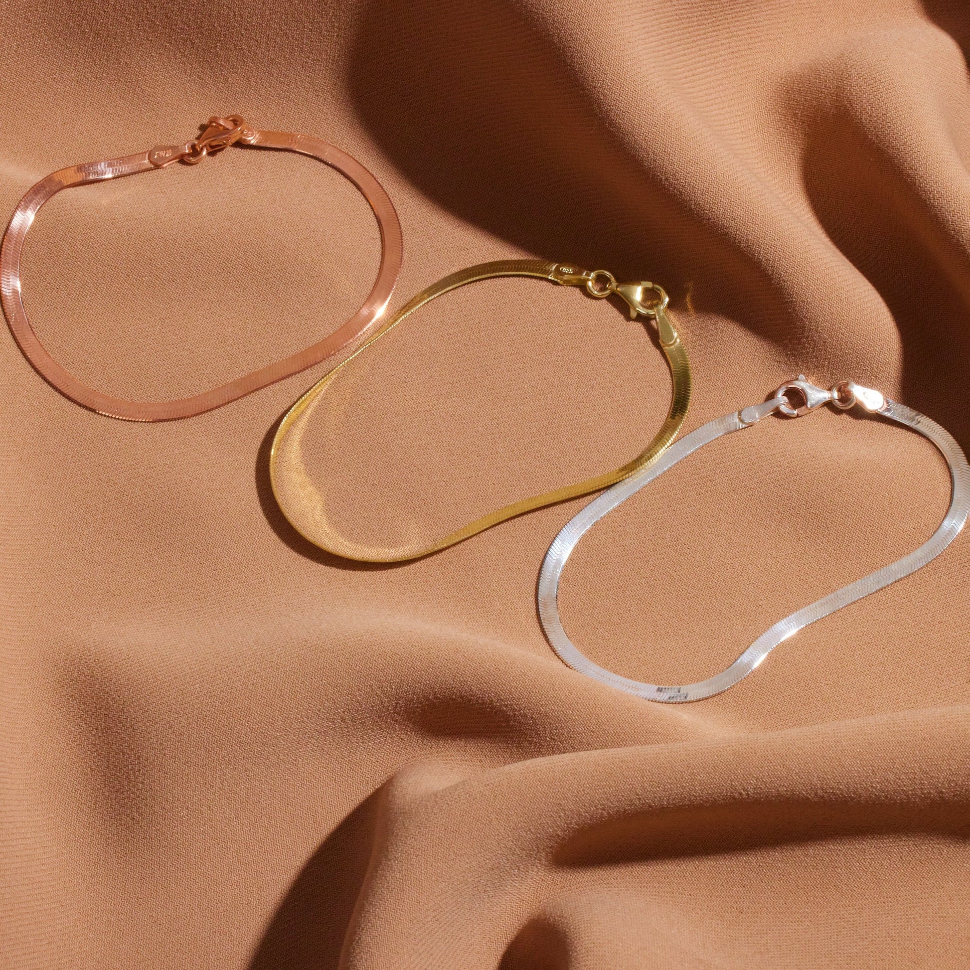 Three hoop earrings in rose gold, gold, and silver on a beige fabric background.