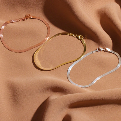 Three hoop earrings in rose gold, gold, and silver on a beige fabric background.