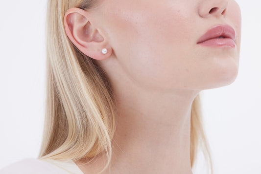 Close-up of a woman wearing pearl earrings with a neutral background
