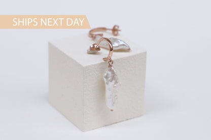 A close-up image of a pair of drop baroque pearl earrings in rose gold hoop.
