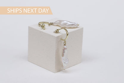 A close-up image of a pair of drop baroque pearl earrings in gold hoop.