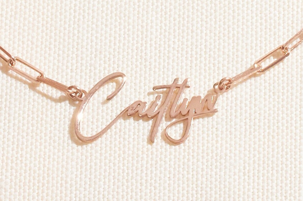 Rose gold name necklace on a light fabric background