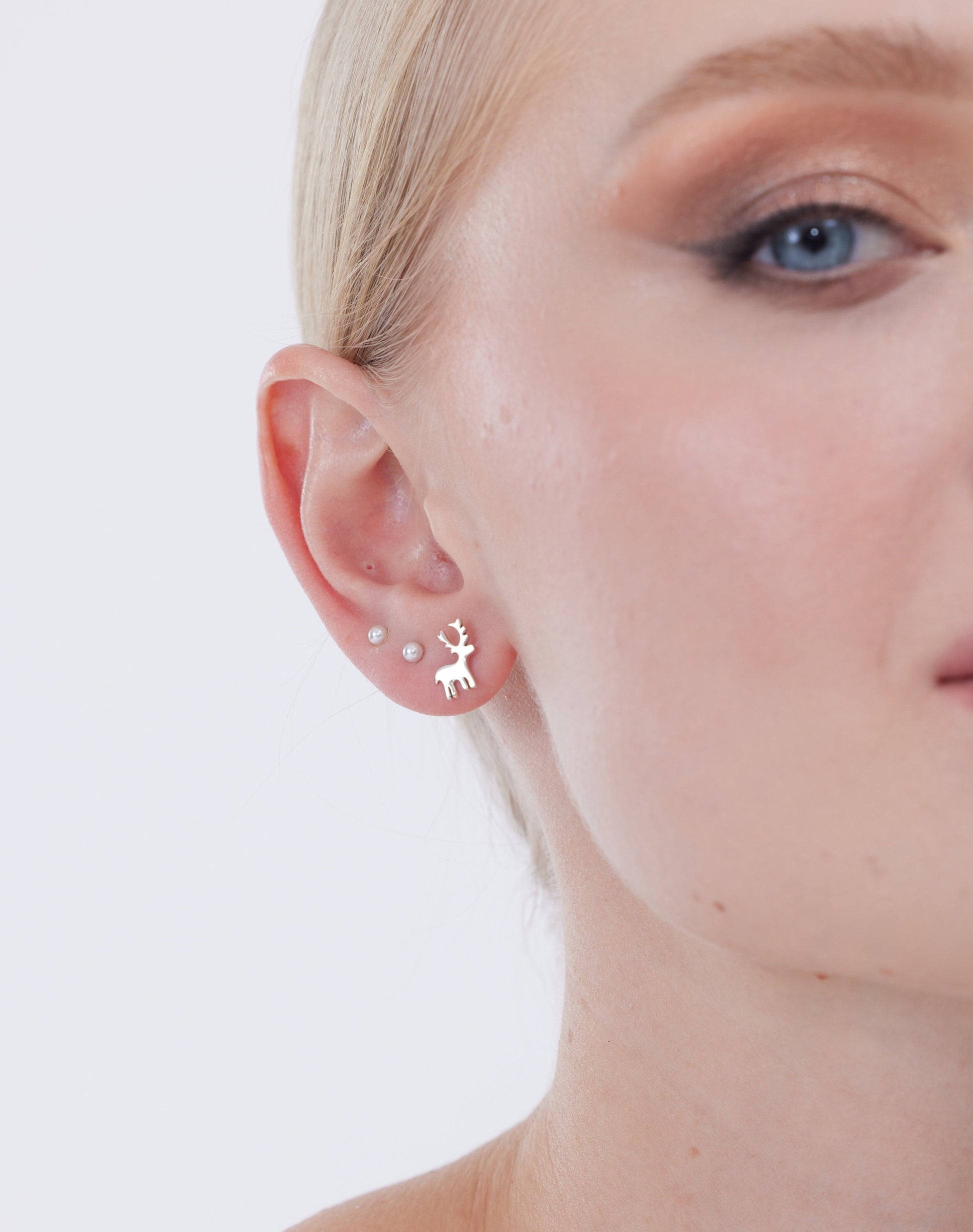 Close-up of a person wearing a silver deer-shaped earring on a white background