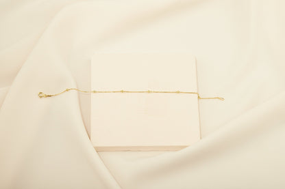 A close-up image of a delicate gold beaded satellite layering necklace that appears to be a choker style.