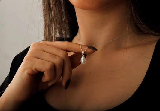 A person wearing a black top holding a dainty freshwater pearl necklace with a gold accent, showcasing its design.