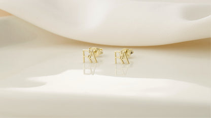 displaying a small stud earring with the letter 'A' on the index finger.