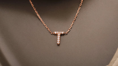 Rose gold necklace with a 'T' pendant on a brown fabric background