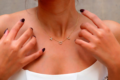A close-up image of a woman's neck wearing a dainty two-initial pave necklace with a heart-shaped charm.