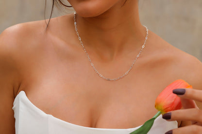 A close-up image of a person wearing a silver loop chain necklace with a delicate and dainty design.