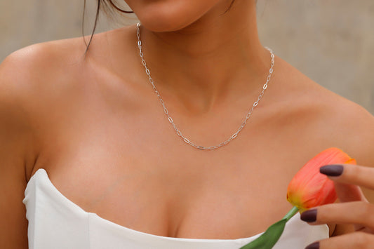 A close-up image of a person wearing a silver loop chain necklace with a delicate and dainty design.