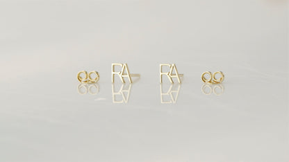displaying a small stud earring with the letter 'A' on the index finger.