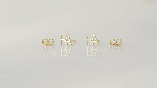 displaying a small stud earring with the letter 'A' on the index finger.