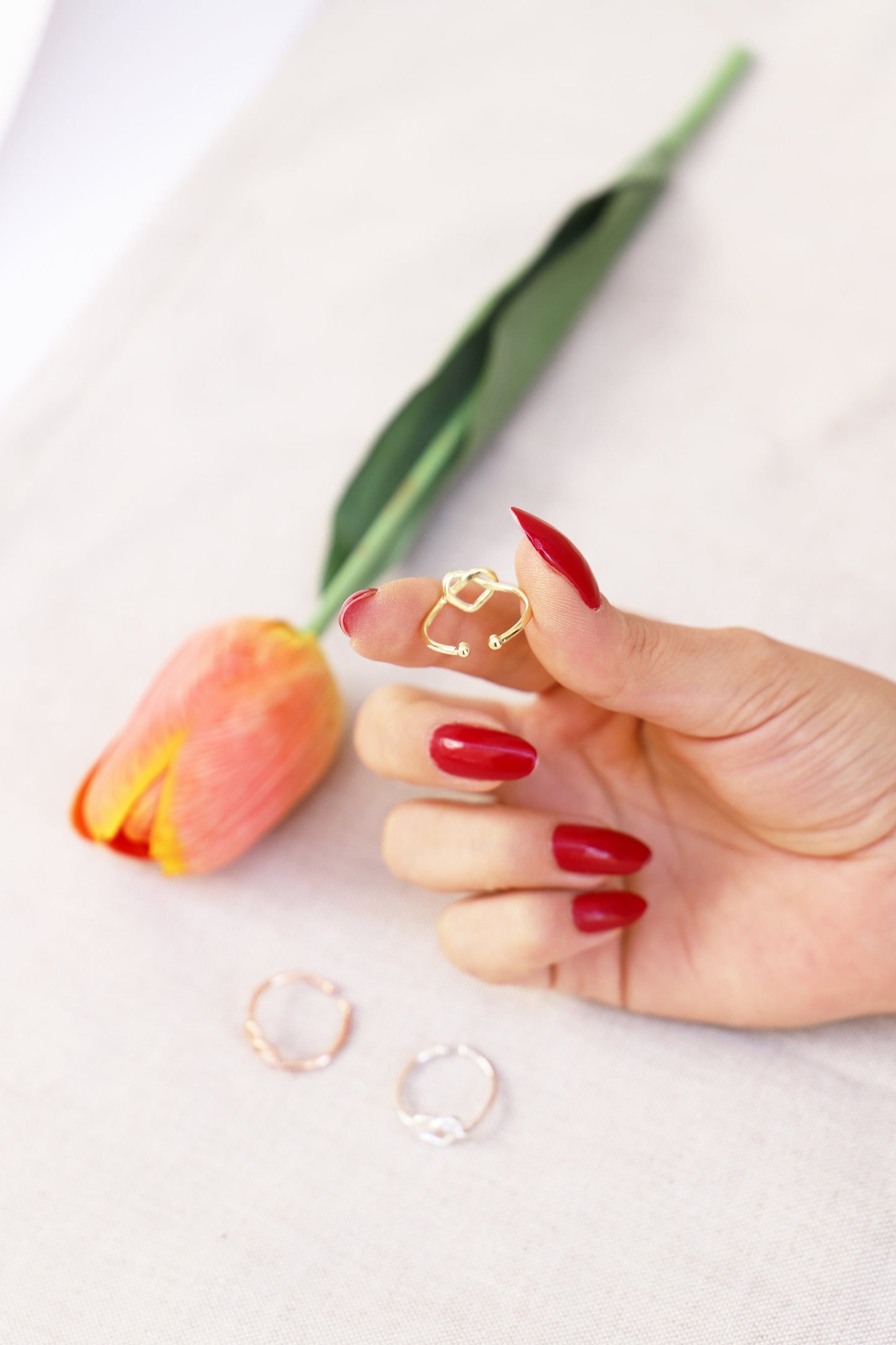 Hand wearing a gold ring with a tulip flower on a white background