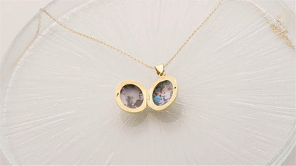 A silver locket necklace with a photo inscribed on it, displayed on a clear glass surface.