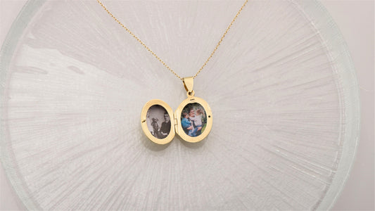 A silver locket necklace with a photo inscribed on it, displayed on a clear glass surface.