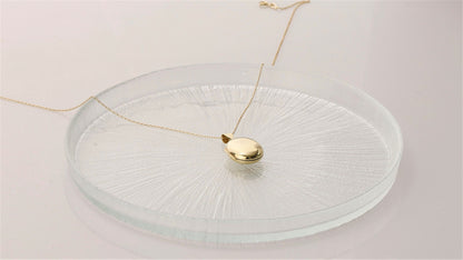 A silver locket necklace, displayed on a clear glass surface.