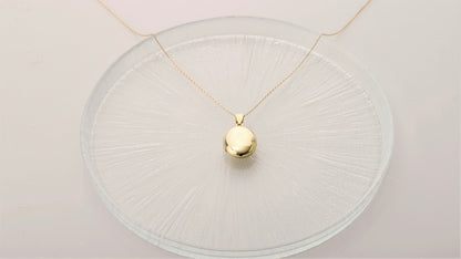 A silver locket necklace, displayed on a clear glass surface.