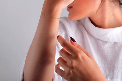 A woman's wrist wearing a dainty 14K gold satellite chain bracelet.