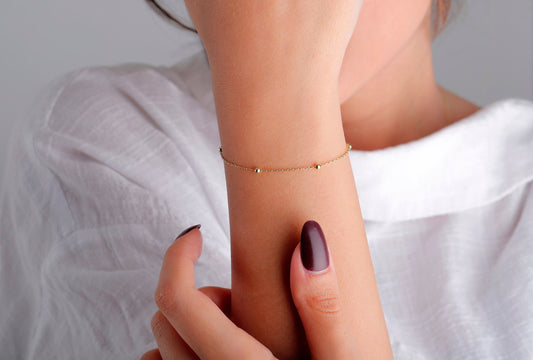 A woman's wrist wearing a dainty 14K gold satellite chain bracelet.