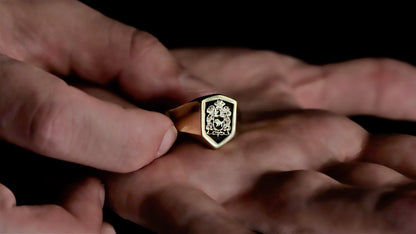 Close-up of a hand holding a gold ring with a emblem design against a dark background