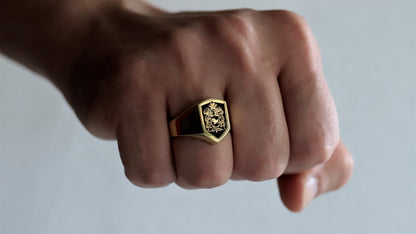 Gold ring with a design on a person's knuckle against a neutral background