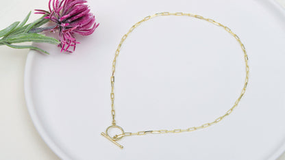 A close-up image of a woman wearing a black tank top showcasing an 18k gold link chain necklace with a paperclip design and a sailor clasp.