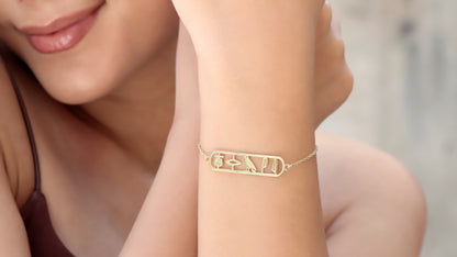 A person wearing a gold-colored bracelet with the hieroglyphic design 'Anubis Bastet Sekhmet' on their wrist.