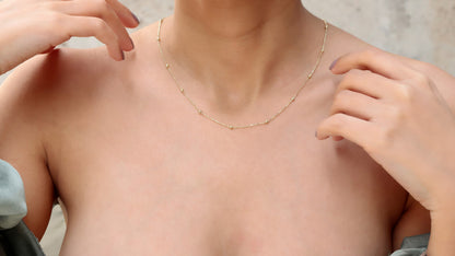 A close-up image of a woman wearing a delicate gold beaded satellite layering necklace that appears to be a choker style.