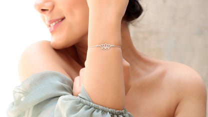 A woman wearing a dainty gold bracelet with a lotus flower design on her wrist.