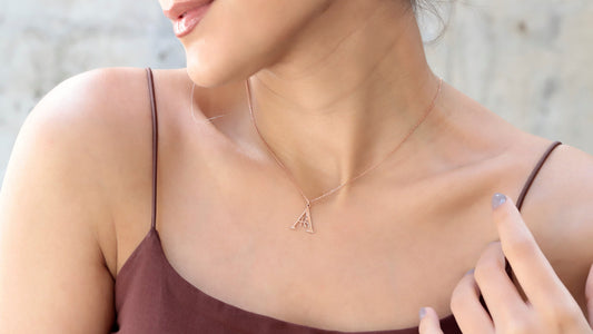 A rose gold-colored necklace with a pendant in the shape of a letter 'AR' on a person's neck.