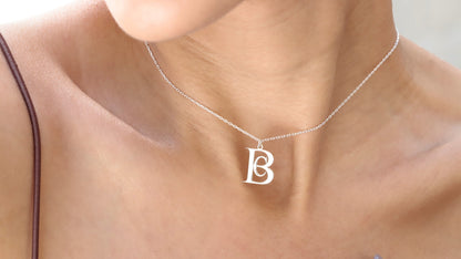 A gold-colored necklace with a pendant in the shape of a letter 'BC' on a person's neck.