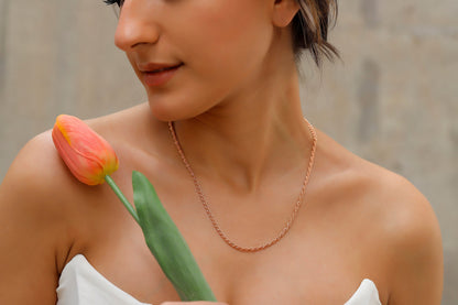 A person showing a rose gold twist chain necklace with a silver rope chain design, worn around the neck.