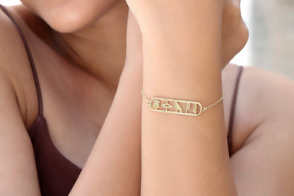A person wearing a gold-colored bracelet with the hieroglyphic design 'Anubis Bastet Sekhmet' on their wrist.