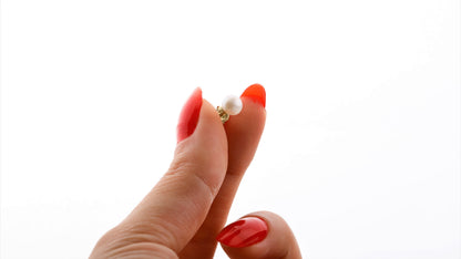 A pair of gold-colored pearl stud earrings placed on a white surface.