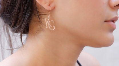 A close-up image of a woman's ear wearing a dangle earring with the initials 'K' and 'G' IN ROSE GOLD.