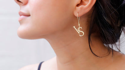 A close-up image of a woman's ear wearing a dangle earring with the initials 'V' and 'S'.