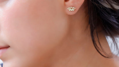 A person wearing a 14K gold dainty lotus flower stud earring in their ear.