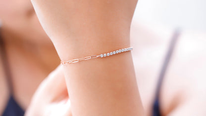 A close-up image of a person's wrist wearing a gold-colored half tennis half link chain bracelet with dainty CZ white diamonds.