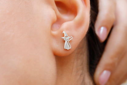 A close-up image of a person's ear wearing a sterling silver stud earring in the shape of a cat.