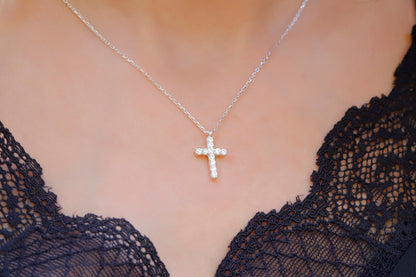 A close-up image of a person wearing a 14K gold diamond cross necklace with a delicate chain, displayed against a lacy black background.