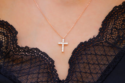 A close-up image of a person wearing a 14K gold diamond cross necklace with a delicate chain, displayed against a lacy black background.
