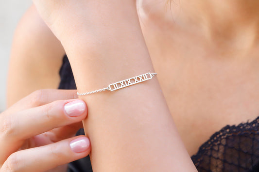 A sterling silver bar bracelet with Roman numerals engraved on it, worn on a person's wrist.